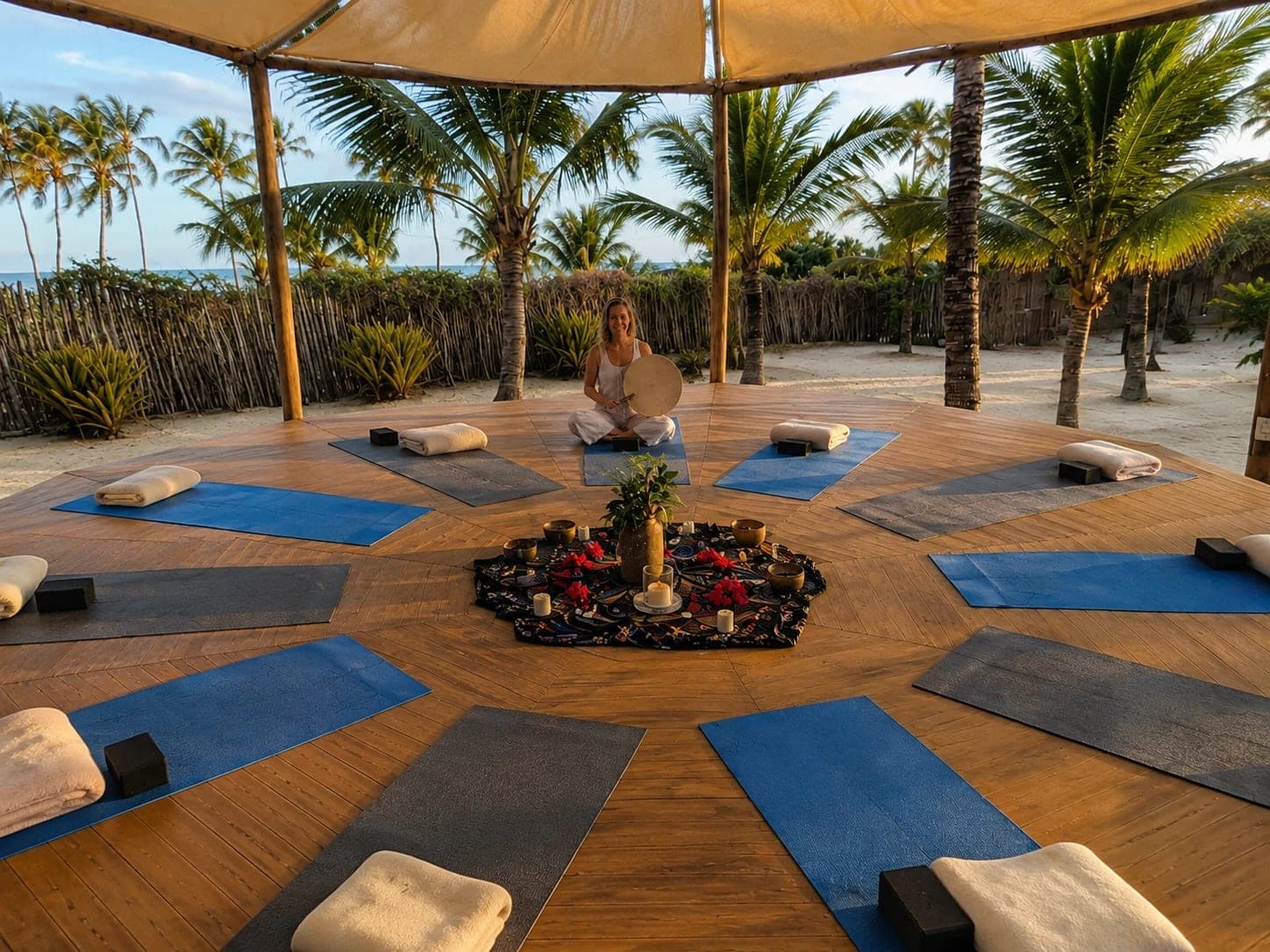 Mats arranged in a circle around an altar on a beach deck, with Bettina holding a frame drum